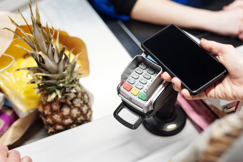 pexels photo 4199526 Close-up of a customer using a smartphone for contactless payment at a retail checkout with a pineapple on the counter.